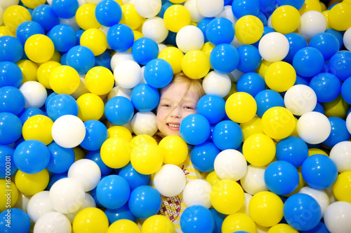 Happy little girl having fun in ball pit in kids indoor play center. Child playing with colorful balls in playground ball pool. photo