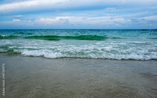 wave of green ocean on sandy beach and blue sky