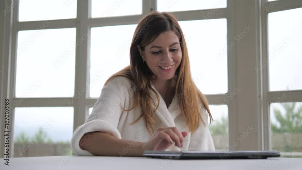 A cheerful woman in a white dressing gown with a tablet at the window. A cheerful woman in a white dressing gown with a tablet at the window.