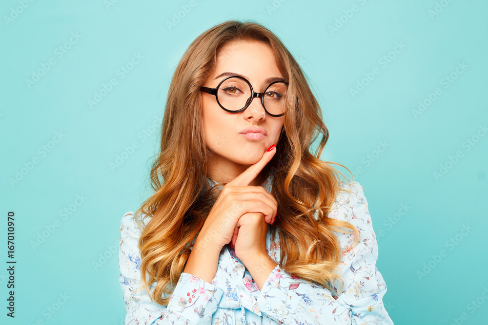 Portrait of a thoughtful girl wearing glasses. Pretty student over blue background Portrait of a thoughtful girl wearing glasses. Pretty student over blue background