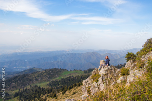 Young woman sitting on a rock and looking at beautiful mountains. Back view. Tourism concept background.