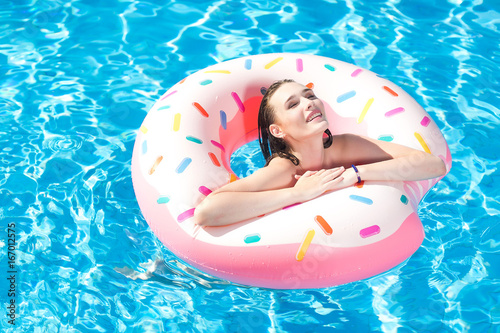 Young caucasian white beautiful woman relaxing in swimming pool. Sexy girl swimming with inflatable ring, smiling and having fun in aquapark. Summer vacation and active holiday concept.