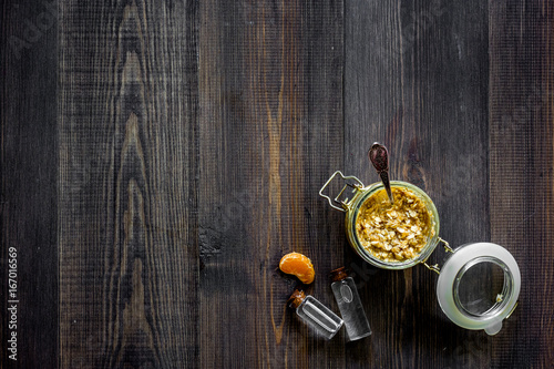 Homemade organic scrub in glass jar, oranges slice and oil on dark wooden background top view copyspace