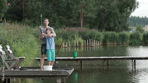 Father teaching son to cast fishing rod on lake photo