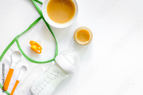 Preparing to feed baby. Puree, spoon, nipple, bottle and bib on white background top view copyspace