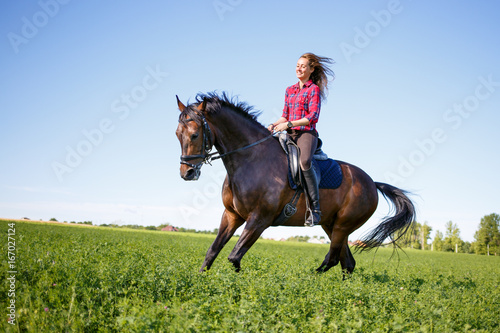 Happy young woman galloping horseback on field and enjoying feeling of freedom