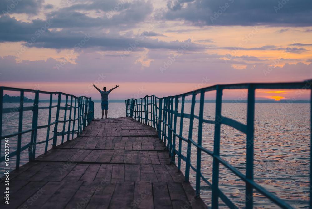 Fototapeta premium man standing on the pier and looking on sunset