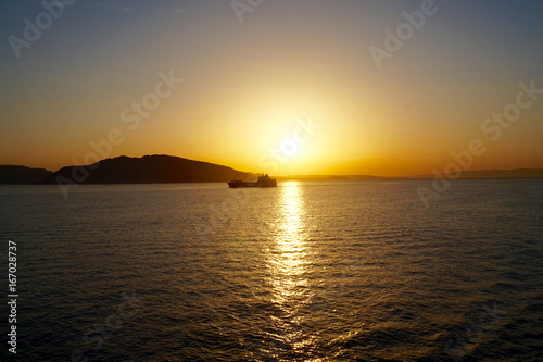 a sunrise on the Aegean sea , while a ship cross the sun's golden path !
