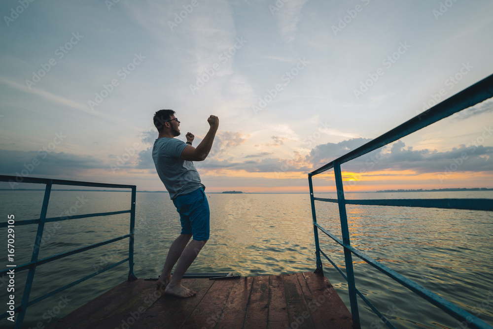 Fototapeta premium man rises hands up on the lake pier