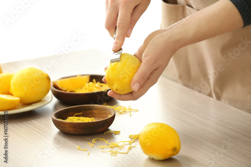 Woman taking off lemon peel with zester over table