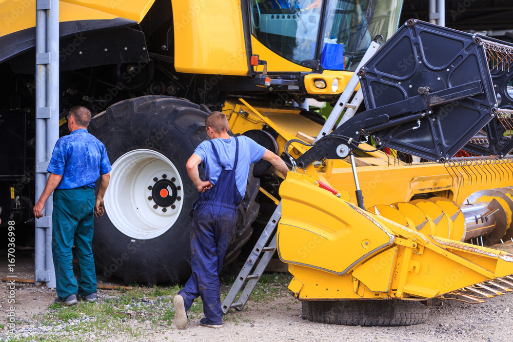 The mechanics repair the yellow Combine harvester in the farm yard. Concept theme repair, mechanics, production, industry, agribusiness company, production of food and agricultural production. The mechanics repair the yellow Combine harvester in the farm yard. Concept theme repair, mechanics, production, industry, agribusiness company, production of food and agricultural production.
