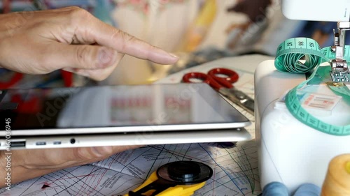 Seamstress working in her studio and browsing internet on tablet
