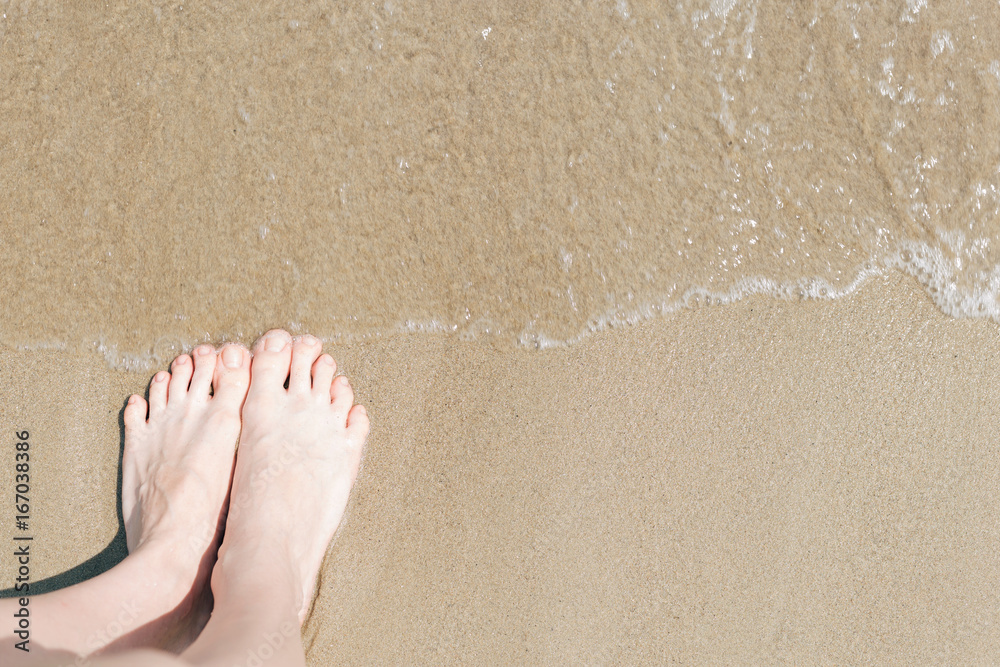 Woman's foots on the yellow sand in the sea