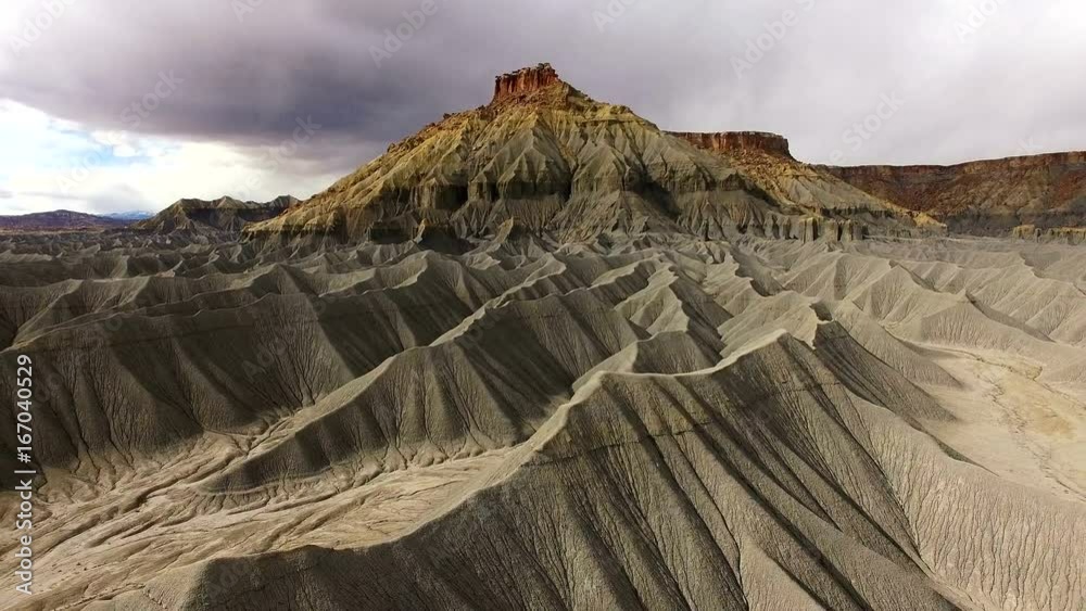 Flying over desert terrain showing sandy hills at the base of a mesa in the Utah badlands.