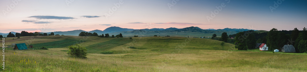 Fototapeta premium Panoramic view of a field and distant mountains at sunrise
