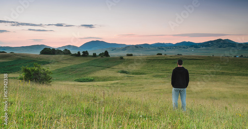 Konstfotografi Man standing in the meadow, watching colors of the sunrise