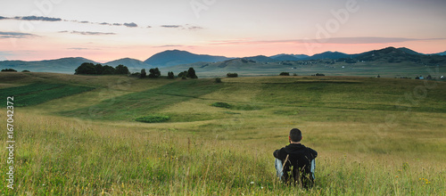 Cuadro en lienzo Man sitting in the meadow, watching colors of the sunrise