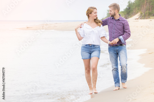 Young couple in love walking along the sea on the beach holding hands and hugging on summer evening © elinque