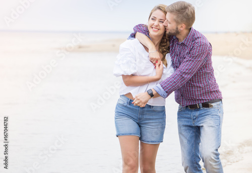 Young couple in love walking along the sea on the beach holding hands and hugging on summer evening