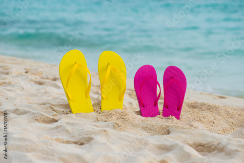 Yellow and pink sandals stand in the sand against the background of the sea.