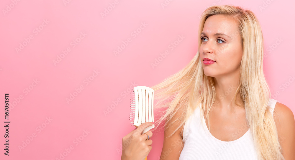 Beautiful woman holding a hairbrush on a pink background Beautiful woman holding a hairbrush on a pink background