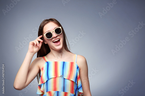 Young emotional girl wearing sunglasses, on grey background