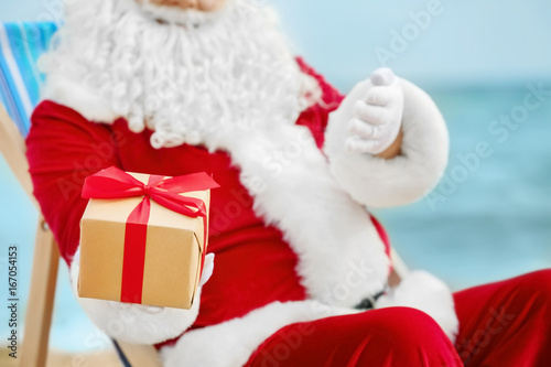 Authentic Santa Claus with gift box in deck chair on beach