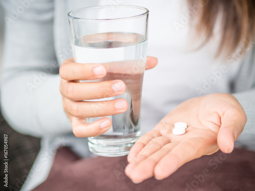 Closeup woman hand with pills medicine tablets and glass of water for headache treatment. Healthcare, medical supplements concept
