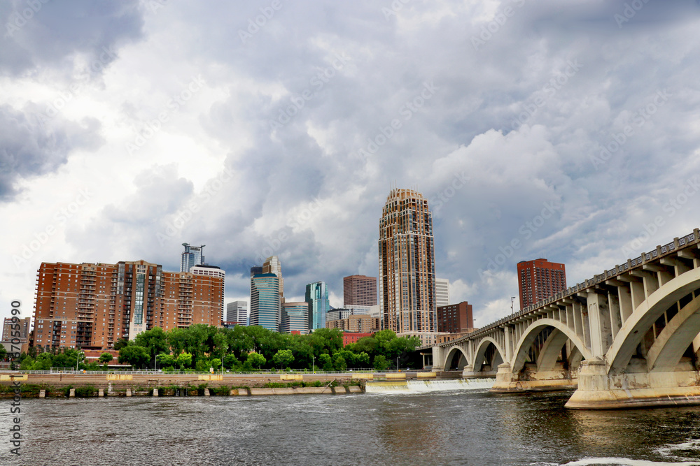 Naklejka premium Cloudy morning in Minneapolis. Minneapolis downtown skyline and Third Avenue Bridge above Saint Anthony Falls, Mississippi river. Midwest USA, Minnesota state.