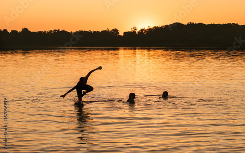 Kids and families are having fun at a lake under sunset