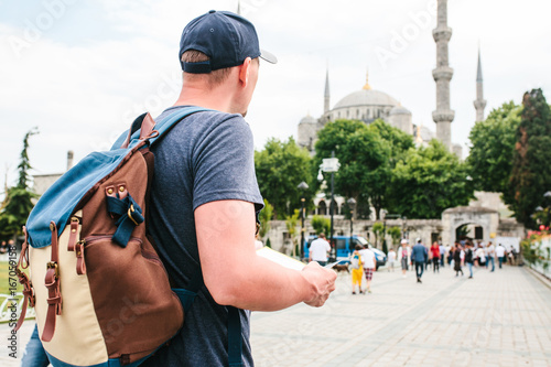 Photography A traveler in a baseball cap with a backpack is looking at the map next to the blue mosque - the famous sight of Istanbul