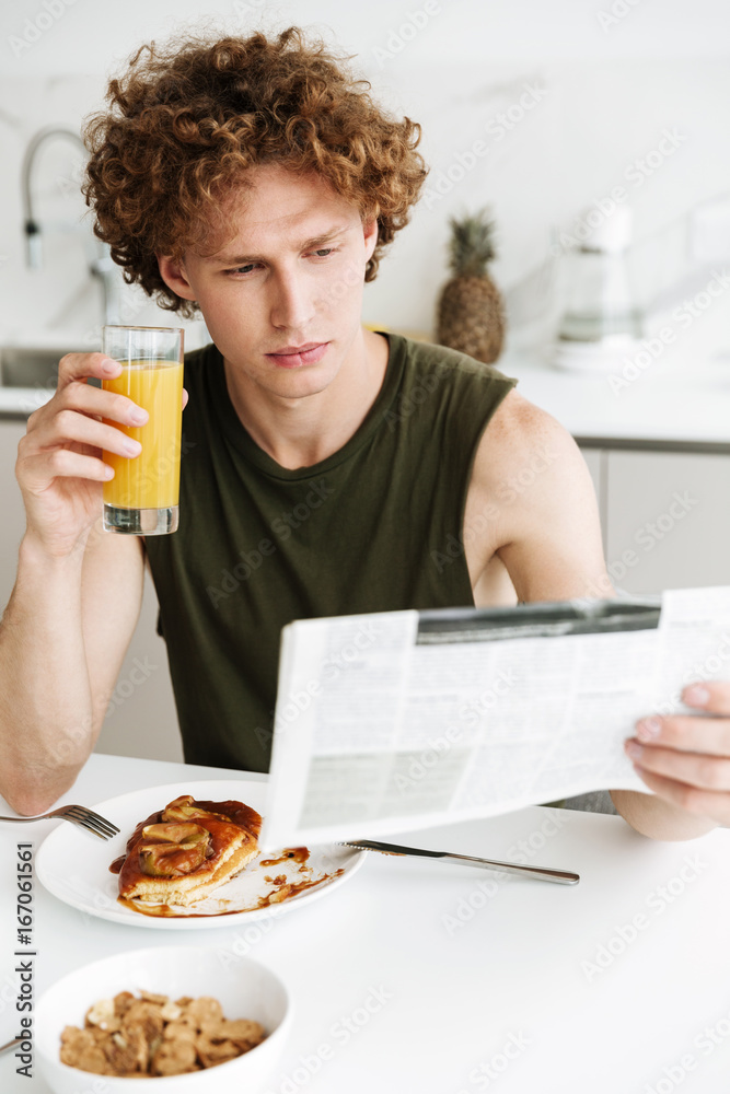 Handsome serious man holding newspaper and drinking juice Handsome serious man holding newspaper and drinking juice