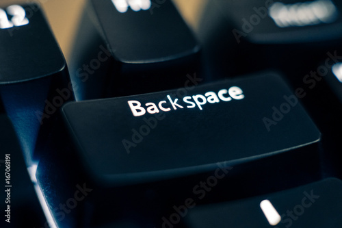 Macro photo of the backspace key on a mechanical switch keyboard. The letters are etched on black plastic ABS keycaps to reveal the white led backlight. Other keys are out of focus in the background. photo