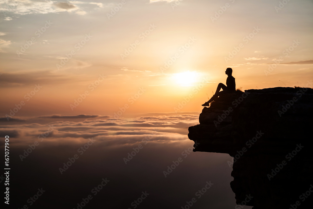 Woman sitting on the cliff and enjoying sunset