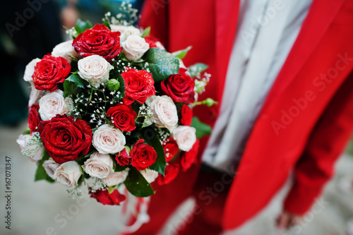 Close-up photo of groom holding wedding bouquet consisting of red and white roses.