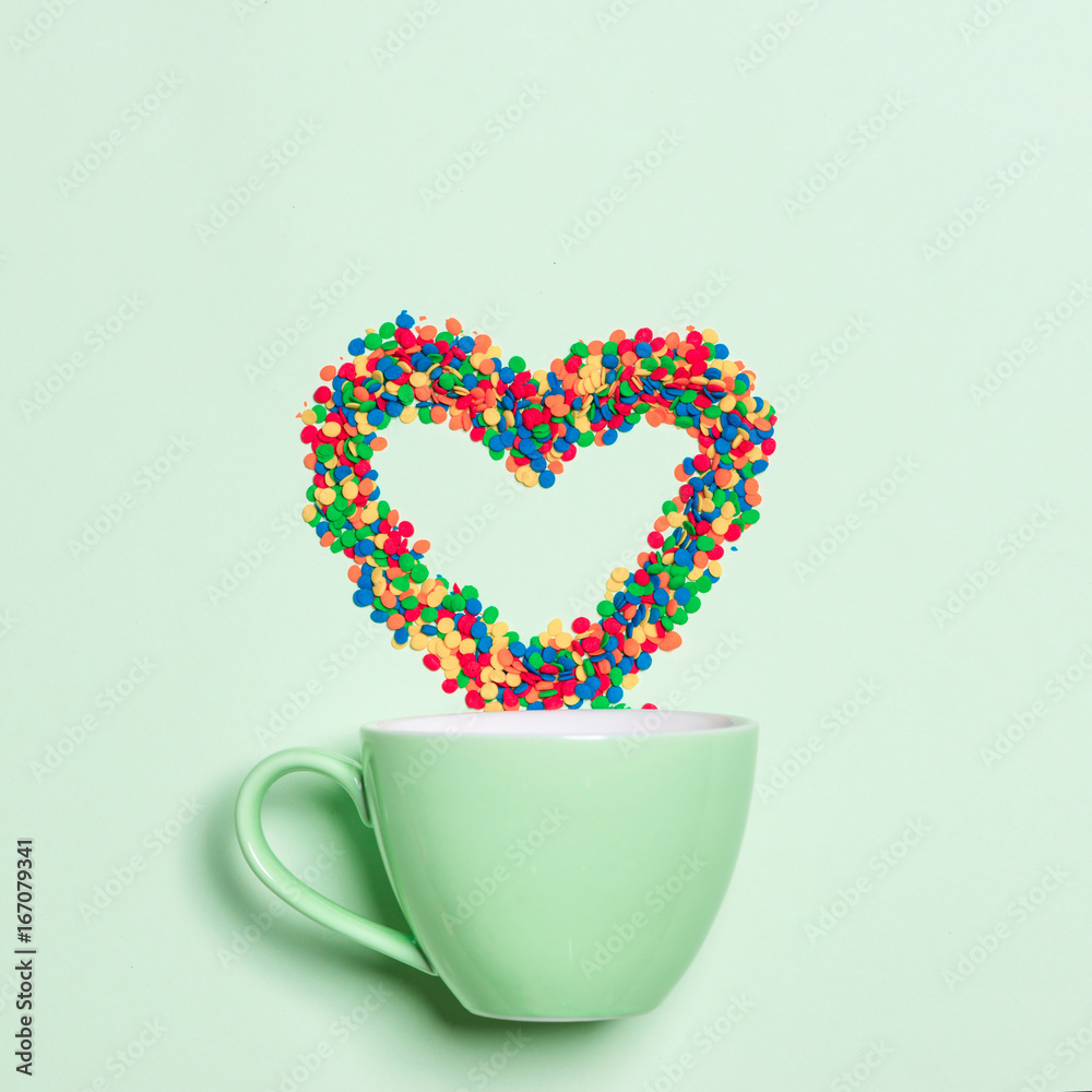 Cup of Cappuccino with heart shape symbol and candy on pastel green background Cup of Cappuccino with heart shape symbol and candy on pastel green background