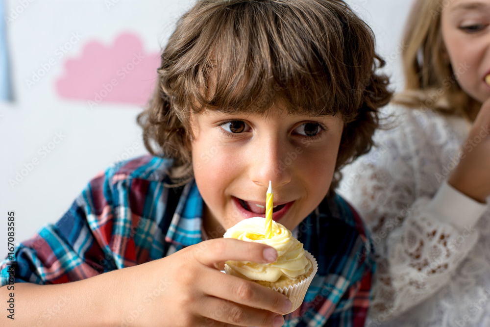 cute smiling boy eating cupcake with candle at birthday party cute smiling boy eating cupcake with candle at birthday party