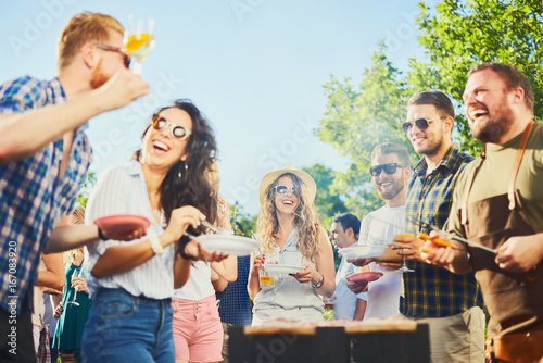 Canvas Print Small group of people standing around barbecue grill at outdoor party