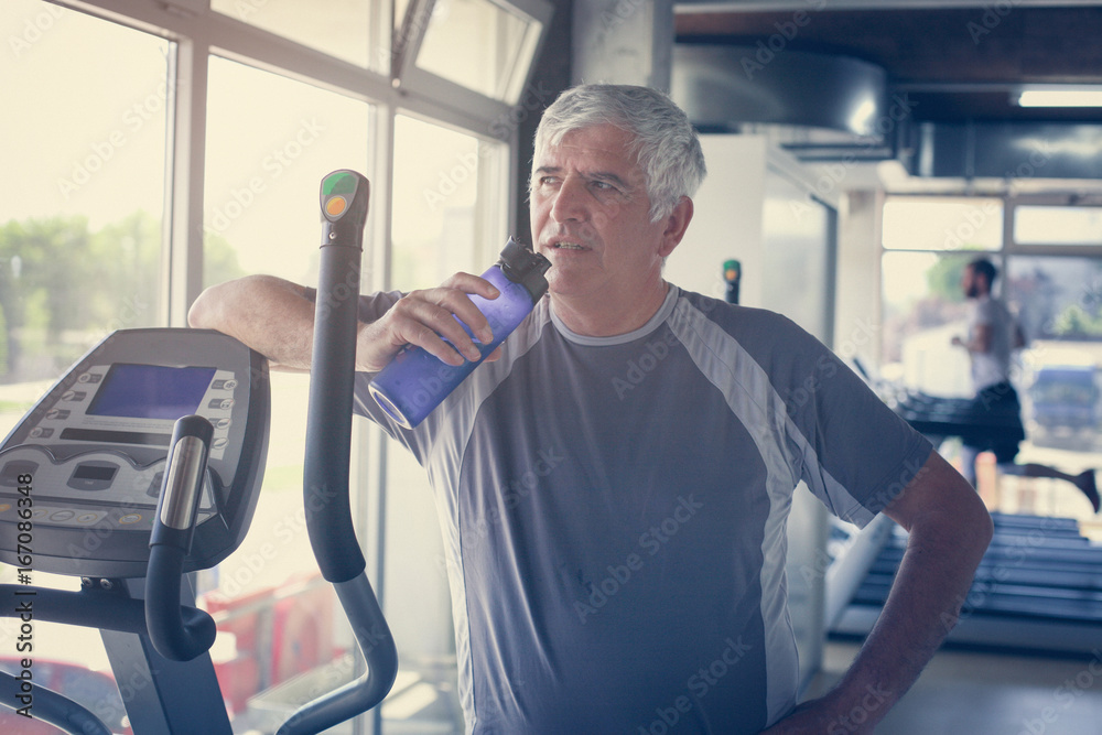 The elderly man holding a bottle of water. The man is refreshed water after exercise at the gym. Man workout in gym.