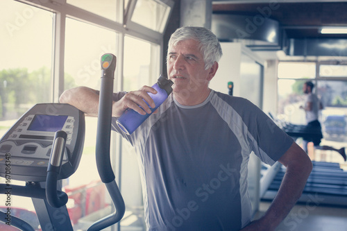 The elderly man holding a bottle of water. The man is refreshed water after exercise at the gym. Man workout in gym.