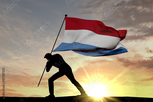Luxembourg flag being pushed into the ground by a male silhouette. 3D Rendering