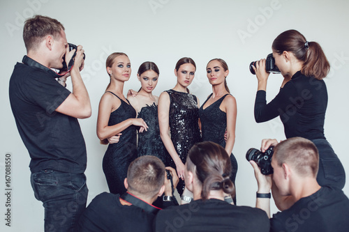 Photographers paparazzi take photos of women in cocktail dresses.