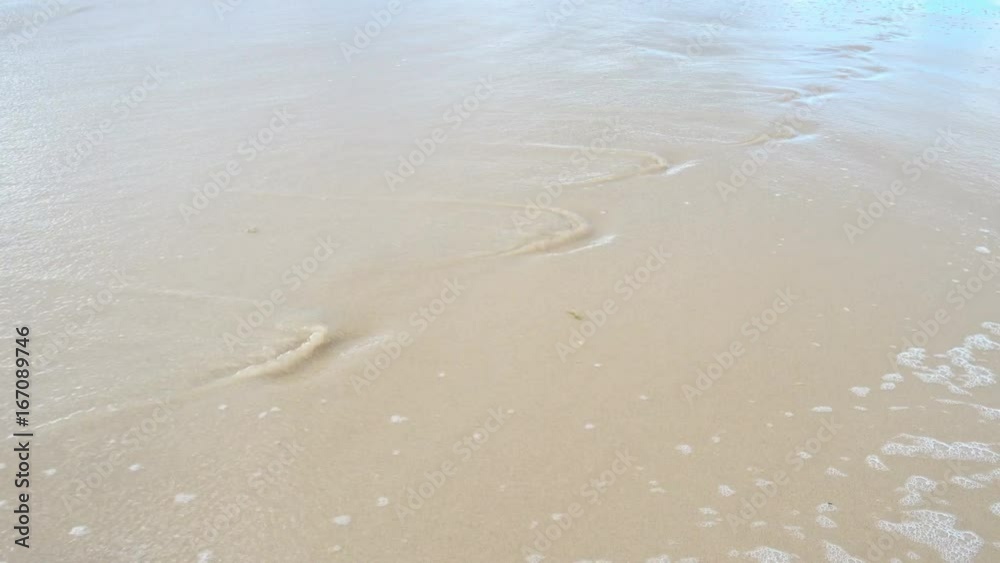 Waves crashing on shore wipe away footprint in the sand on beach Waves crashing on shore wipe away footprint in the sand on beach