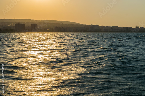 The silhouette of the city of Novorossiysk at sunset and the reflection of sunset in the waves of the uneasy Black sea