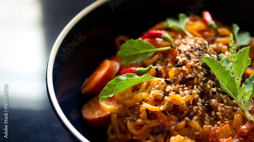 Hot and spicy instant noodle with basil and chili in dark-blue bowl on black background.  Side view.