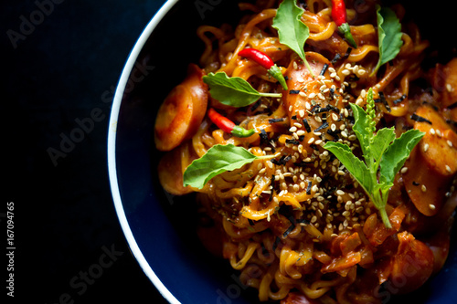 Hot and spicy instant noodle with basil and chili in dark-blue bowl on black background. Top view