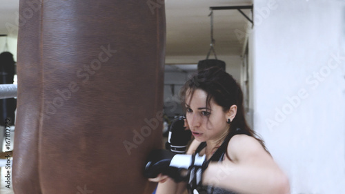 Beautiful female boxer training punching bag in boxing gym. Self defense workout. Motion blur effect.   © Bobboz