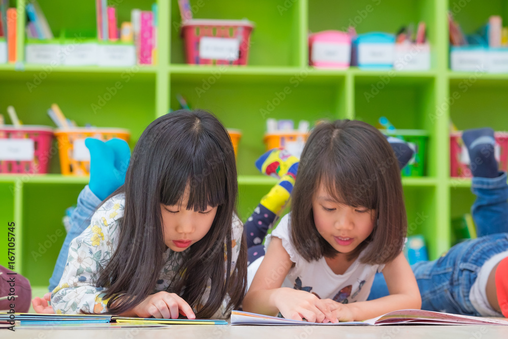 Fototapeta premium Two girl kid lay down on floor and reading tale book in preschool library,Kindergarten school education concept