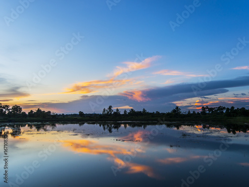 A sunset is reflected symmetrically in a lake in eastern Thailand