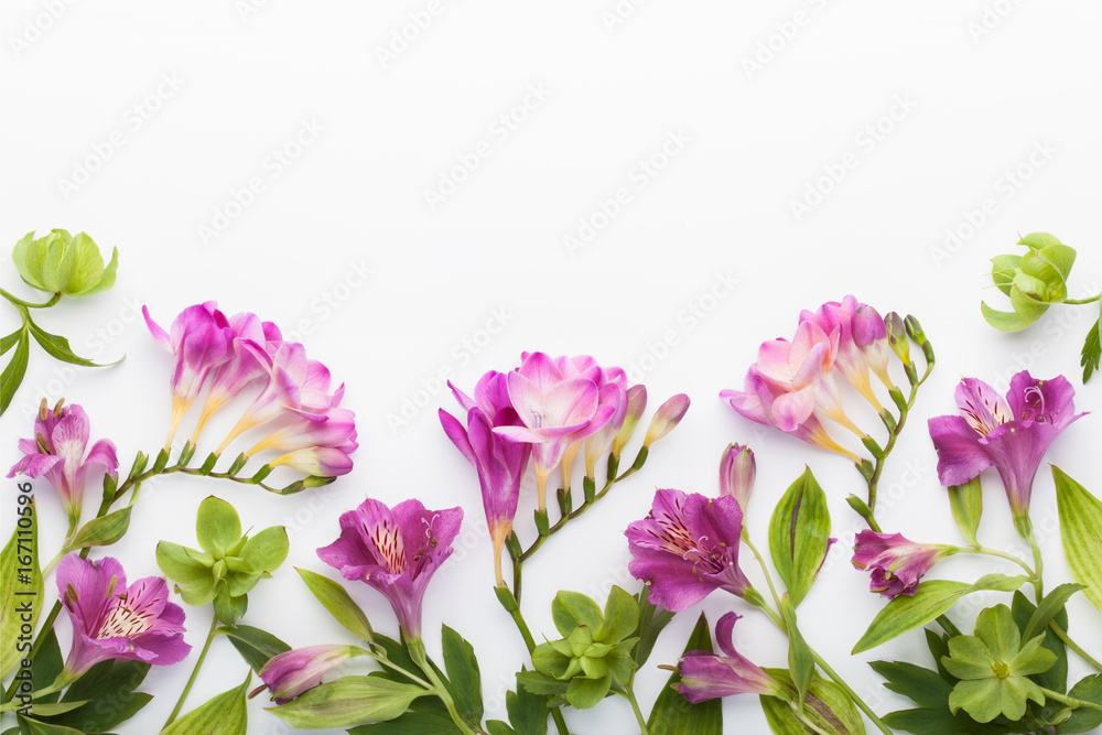 Floral frame made of alstroemerias, freesia flowers and green leaves on white background. Flat lay, top view.